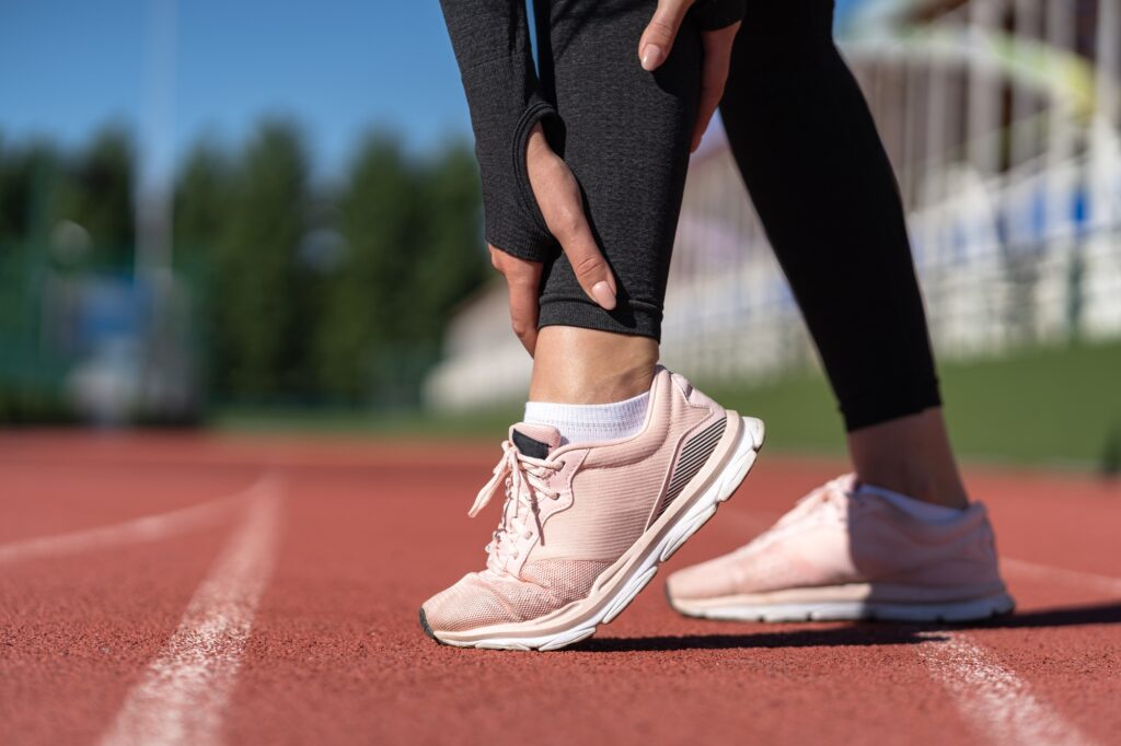 Woman runner on track holding her ankle in pain, indicating a sprained ankle injury, emphasizing sports injury treatment and rehabilitation.