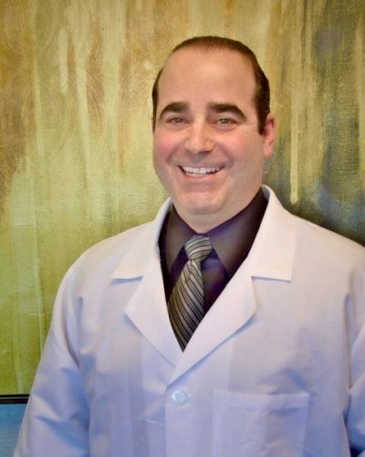 Dr. Brian Opensky, podiatrist in white coat, smiling against a warm background, representing compassionate foot and ankle care at Opensky Podiatry, Inc.